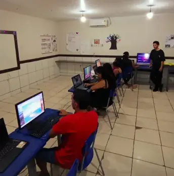 Alunos durante aula prática de informática com acompanhamento do instrutor